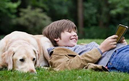 Boy resting on his dog, reading a book
